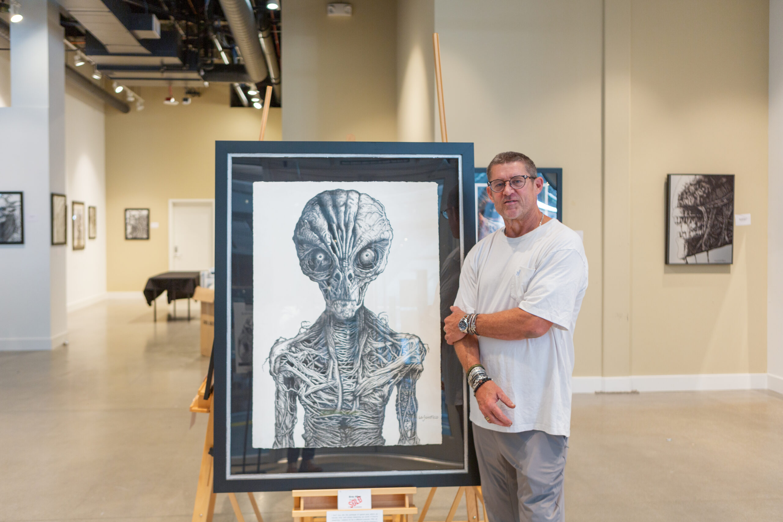 Artist next to his painting at the CREATURES Art Exhibit